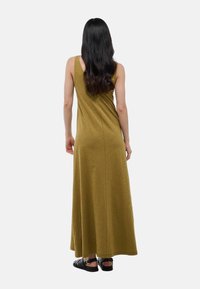 Robe maxi sans manches vert olive avec une coupe décontractée et une texture lisse. Le mannequin se tient de dos, portant des sandales plates noires.
