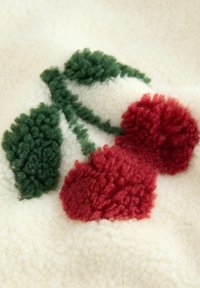 Fleece fabric with an off-white background featuring red tufted cherries and green leaves, creating a textured floral design.