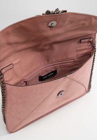 Bolso de mano interior rosa con una correa de cadena, cierre magnético y un bolsillo interior con cremallera y etiqueta de marca. Textura similar al ante.
