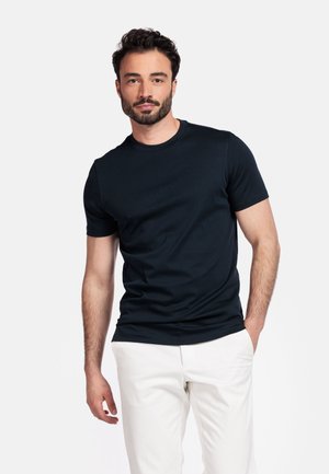 Donkerblauwe katoenen t-shirt met korte mouwen en een ronde hals, gedragen met witte broek. Gladde textuur, getailleerd design.