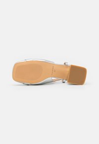 Sandal con tacco bianco con tomaia sintetica argentata, punta quadrata, cinturini trasparenti, suola marrone uniforme e fondo texturizzato per una migliore aderenza.