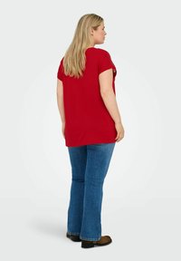 Rød kortærmet tunika med en rund kant, parret med blå udvidede jeans. Stoffet ser blødt ud med en afslappet pasform.
