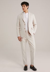 Helle beige Leinenanzug mit taillierter Passform, einreihiger Blazer mit zwei Knöpfen und schrägen Taschen, ergänzt durch ein weißes Hemd.