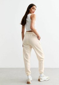 Pantalones de chándal color beige claro con puños y cinturilla elásticos. Combinados con zapatillas blancas y un top corto blanco. Textura suave.
