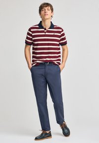 Burgundy- och creamrandig polo-skjorta med marinblå krage, ihopparad med marinblå byxor och mörka skor. Outfitten har en avslappnad design och en figursydd passform.