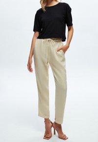 T-shirt noir court à manches courtes associé à un pantalon crème à taille élastique avec un cordon de serrage et des revers, complété par des talons beiges.