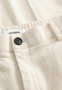 Ecrü színű farmernadrág fekete gombbal és a derékpánton látható, "GABBA" márkajelzésű felirattal.