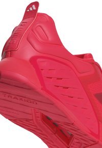 Scarpa sportiva rossa con suola in gomma testurizzata, collare imbottito e linguetta sul tallone, caratterizzata da un design geometrico distintivo e branding.