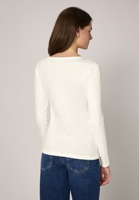 Witte longsleeve met een ronde hals en geribbelde structuur, gecombineerd met blauwe spijkerbroek met achterzakken en een rechte pijp.
