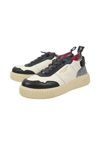 Sneakers in tela texture con una base crema, dettagli in pelle nera e un tallone decorato. Presentano lacci scuri e suole in gomma.