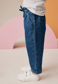 Pantaloni jogger in denim blu scuro, con vita elastica e laccetto, tasche laterali e orli a sigaretta; abbinati a sneakers bianche.