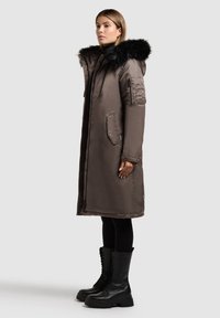 Brun polstret frakke med en faux fur hætte, der har lynlåslommer og en lang silhuet. Bæres med sorte højhælede combat støvler.