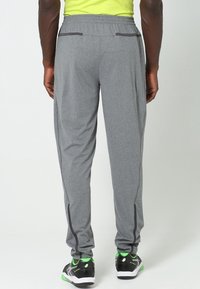 Šedé sportovní kalhoty s tapered střihem, vyrobené z lehké látky, s kontrastními tmavými švy a zipovými otvorami na kotnících.