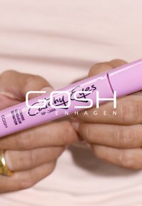 Rosa mascaratub med böjd design, märkt "Catchy Eyes," med svart text och en glänsande finish, hålls i händer.