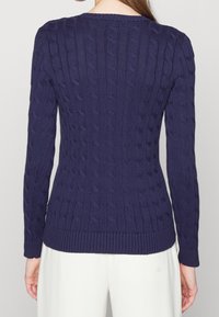 Marinblå kabelstickad tröja med långa ärmar, ribbat halsringning och nederkant, med ett strukturerat mönster över hela ryggen.