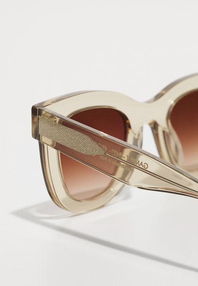 Transparent light brown sunglasses with oversized cat-eye shape, gradient brown lenses, and patterned temple detailing.