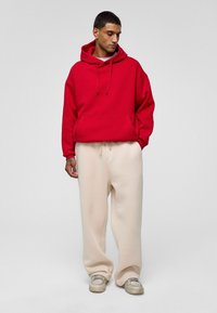 Rode hoodie met een voorzak en een trekkoordcapuchon, gecombineerd met losse beige sweatpants en grijze sneakers. Glad materiaaltextuur.