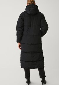 Zwarte pufferjas met een capuchon, met een lange silhouet, verdeeld in horizontale secties, en een gestructureerde stof.