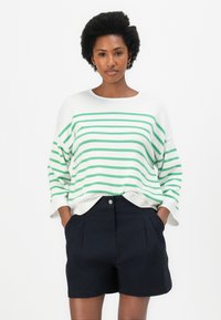 Weißer Strickpullover mit grünen Streifen, weiten Ärmeln und geripptem Saum, kombiniert mit hochtaillierten marineblauen Shorts mit Falten und Fronttaschen.