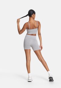 Sivina športna dvodelna kompleta z izrezanim zgornjim delom in tankimi naramnicami ter hlačami z visokim pasom. Vključuje strukturirano tkanino in brezšiven dizajn.