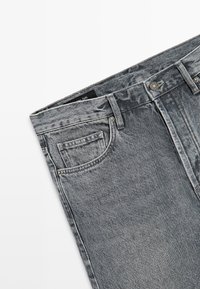 Šedé džíny s vysokým pasem z denimu s přední kapsou, poutečky na opasek a kovovým zapínáním na knoflík na světlém pozadí.