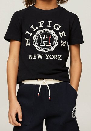 T-shirt en coton noir avec un col rond, des manches courtes et un logo blanc avec des accents rouges. Associé à un pantalon marine à taille élastique avec cordon de serrage.
