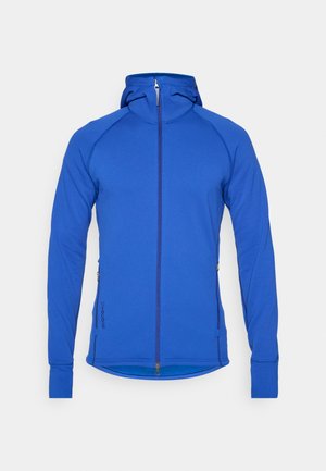 Blå hettejakke med glidelås og tettsittende design, hette og lange ermer. Har sidelommer og ribbestrikkede mansjetter. Glatt stofftekstur.