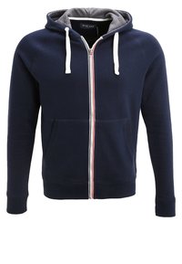 Felpa con zip di colore blu navy, con cappuccio foderato in grigio. Presenta lacci bianchi, una zip a strisce rosse e bianche e tasche frontali.
