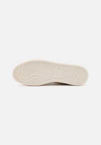 Sneakersåle i lys beige, med et teksturert, sikksakk mønster for grep, med merkevaren synlig i midten.