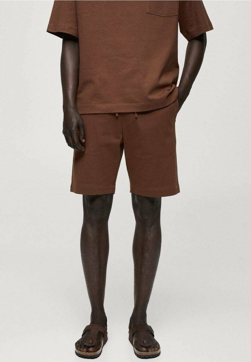 T-shirt en coton marron à manches courtes avec une poche, associé à un short marron assorti avec une taille à cordon. Porté avec des sandales marron.