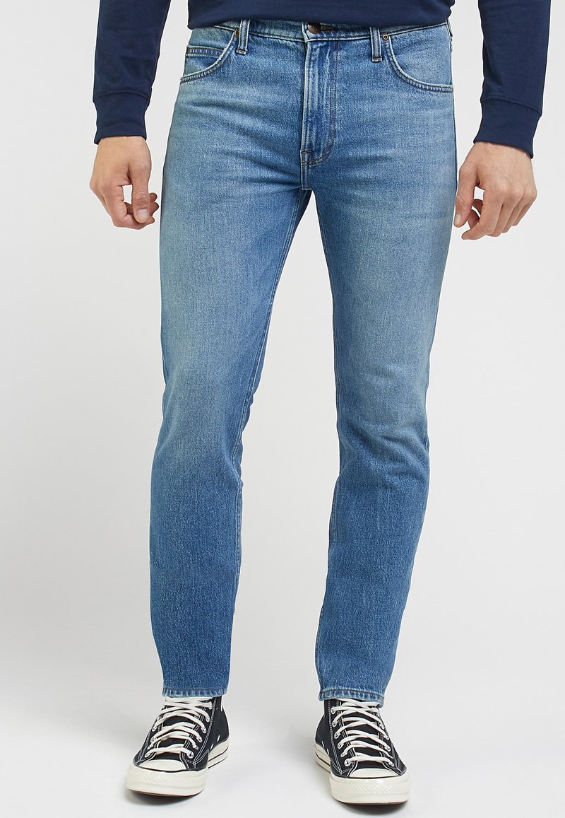 Jasnoniebieskie jeansy o slim fit, z pięcioma kieszeniami i delikatnymi, wyblakłymi elementami; w połączeniu z czarnymi, wysokimi trampkami.