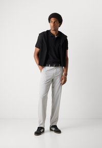 Zwarte poloshirt met een textuurvest, lichtgrijze op maat gemaakte broek en zwarte sneakers met witte strepen. Eenvoudig, modern ontwerp.