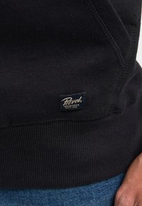 Felpa con cappuccio di colore blu navy a maglia, con polsini e orlo a costine, caratterizzata da un piccolo etichetta Petzl Industries sul lato. Texture morbida, design semplice.