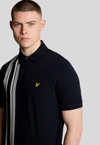 Polo navy con striscia verticale in bianco e navy a contrasto, logo ricamato in oro sul petto e design del colletto classico.