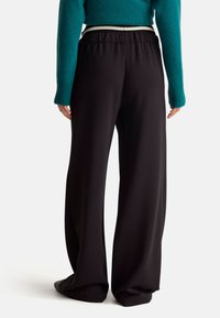 Czarne spodnie z szerokimi nogawkami, z elastycznym paskiem i białymi akcentami, połączone z teksturowanym swetrem w kolorze teal.