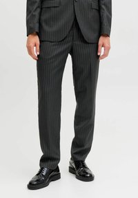 Czarne spodnie w delikatne prążki w dopasowanym kroju, o g�ładkiej fakturze, zestawione z eleganckimi czarnymi butami wizytowymi.