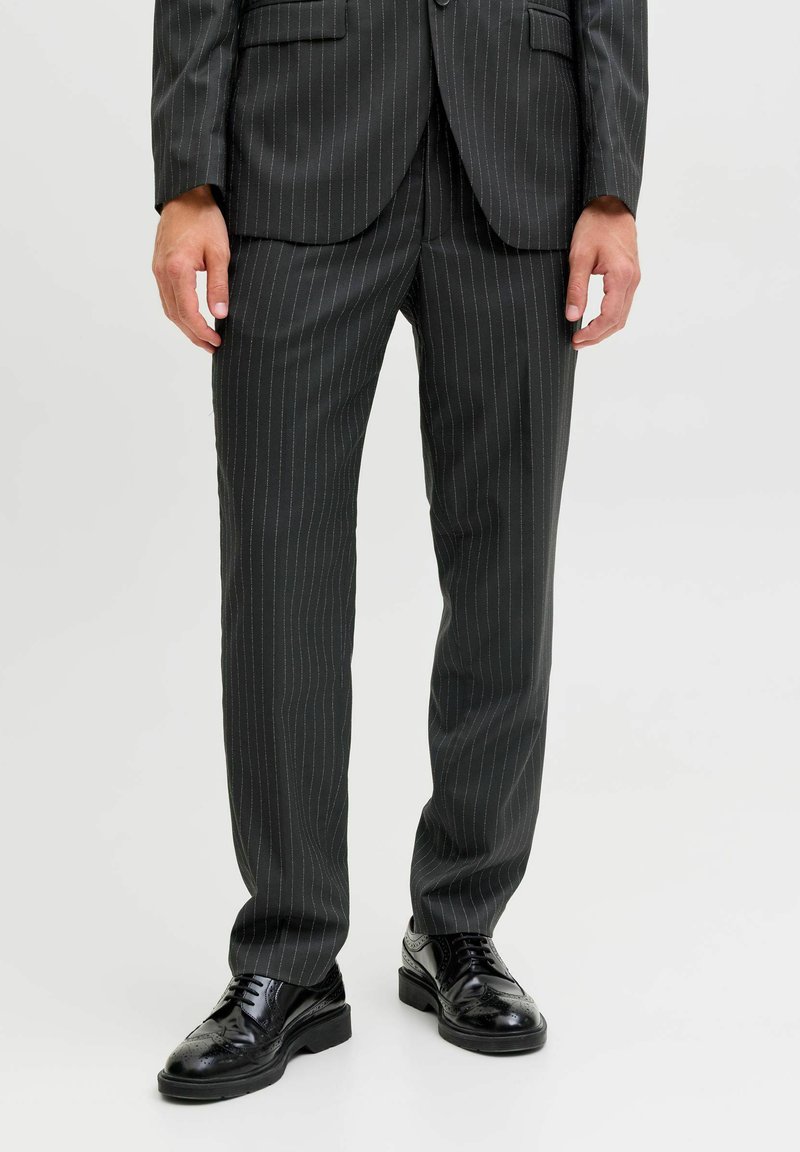 Czarne spodnie w delikatne prążki w dopasowanym kroju, o gładkiej fakturze, zestawione z eleganckimi czarnymi butami wizytowymi.