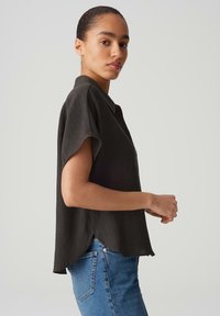 Blusa nera a maniche corte con tessuto texturizzato e chiusura frontale con bottoni, con orlo curvo, abbinata a jeans blu a vita alta.