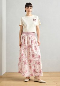 Beige cotton t-shirt with small burgundy graphic on the left chest, paired with a long pink floral patterned skirt and beige flats.