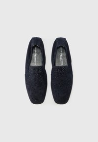 Μπλε σουέντ παπούτσια slip-on με υφή πάνω μέρος που διαθέτει μαύρα τρουκς. Σχεδιασμός με επίπεδη σόλα, στρογγυλή μύτη και χωρίς ορατά κορδόνια.