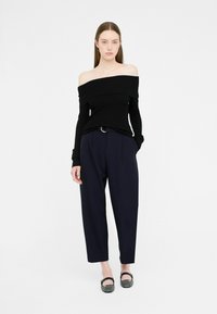 Maglione a spalle scoperte nero in maglia a coste abbinato a pantaloni navy a vita alta con pieghe e ballerine nere texturate con un piccolo dettaglio a fibbia.