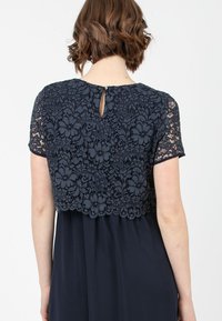 Marinebluse mit kurzen Ärmeln, die mit floralen Motiven verziert ist und einen Schlüsselaugen-Ausschnitt am Rücken hat, kombiniert mit einem einfarbigen marineblauen Rock.