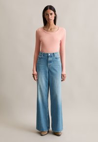 Un haut rose clair à manches longues, à col rond, associé à un jean bleu clair à taille haute et à jambes larges, ainsi qu'à des bottes beiges.