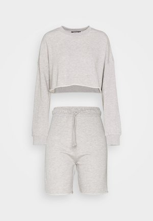 Tenue deux pièces gris clair avec sweat court à manches longues et short taille haute à cordon assorti sur fond uni.
