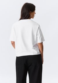 White short-sleeve t-shirt with a round neck, made of smooth cotton fabric, paired with high-waisted black pants featuring back pockets.