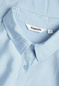 Ljusblå skjorta med knapp-up, mjuk textur, krage och en etikett som säger "Kappahl S." Har två blåa knappar och minimal sömnadsdetalj.