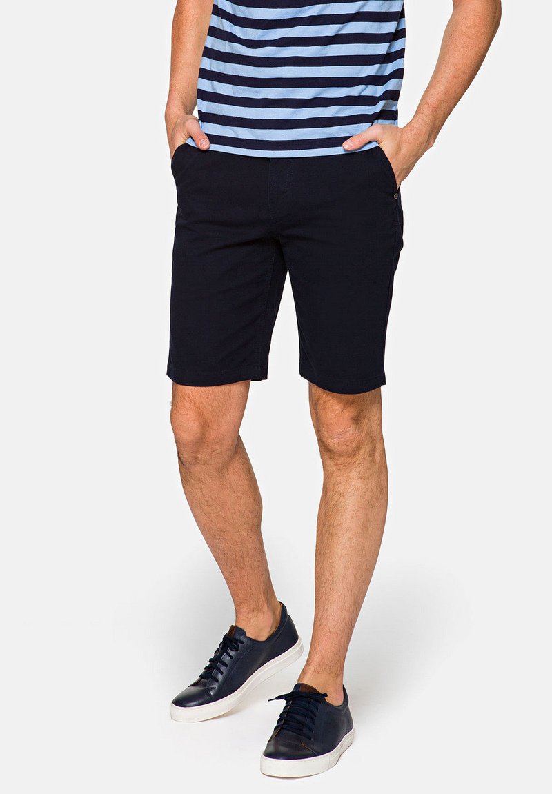 Granatowe szorty wykonane z mieszanki bawełny, z bocznymi kieszeniami i prostym krojem. Połączone z niebieską koszulą w paski i granatowymi trampkami.