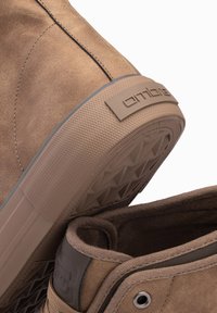 Botas de cuero suede marrón hasta el tobillo con suelas de goma texturizadas y un parche con el logo, que presentan un acabado suave y diseños redondeados.