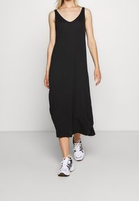 Schwarzes ärmelloses Midikleid mit V-Ausschnitt, aus leichtem Stoff, kombiniert mit weißen Sportschuhen; einfach, lockere Passform.