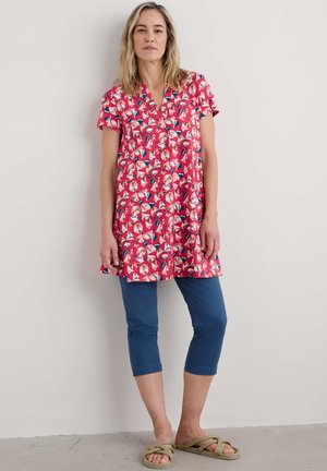 Short-sleeve pink tunic with geometric floral print, paired with blue cropped pants and tan sandals featuring a twisted rope strap.